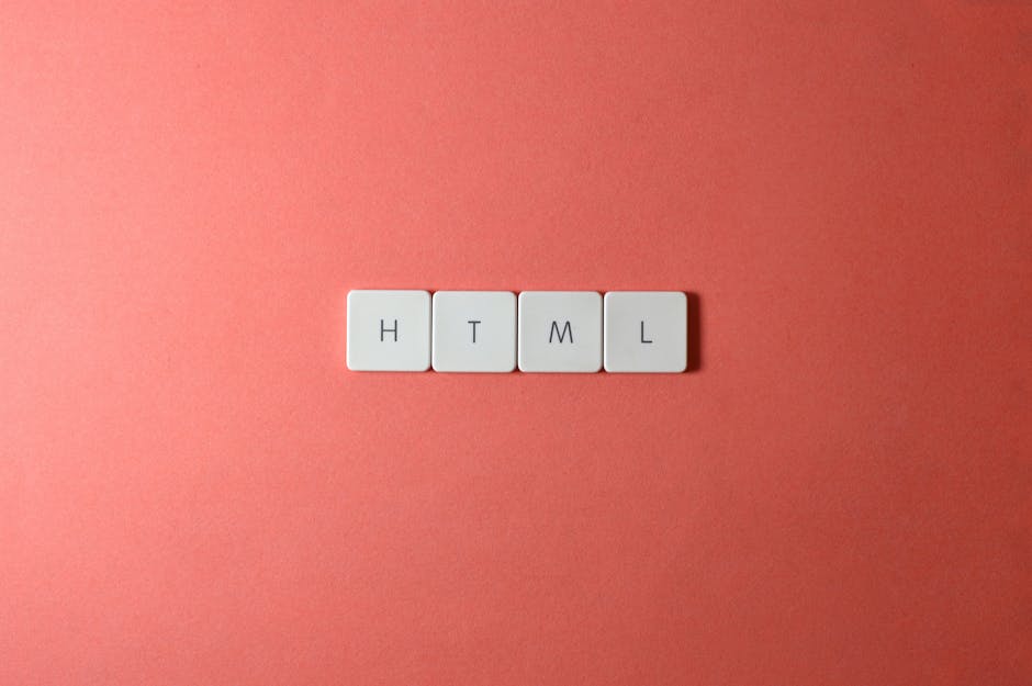 Close-up of four white square tiles with black letters spelling 'HTML' arranged in a straight line on a smooth, coral-pink surface, positioned centrally against a plain background. The lighting is eve