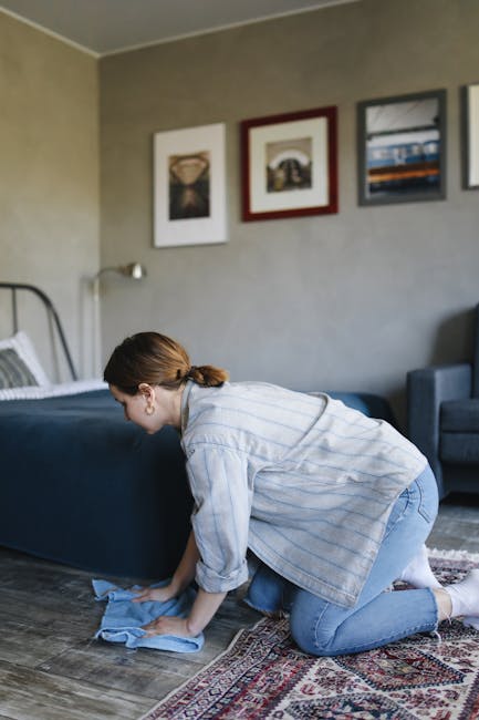Close-up of a vacuum cleaner nozzle attached to a black wand, vacuuming a decorative patterned area rug with floral motifs in soft pastel shades. The rug is situated on a wooden floor, and the scene i